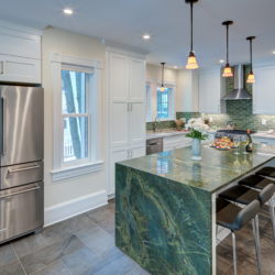 kitchen with large waterfall island, green and white counter tops, green subway tile, and white cabinets