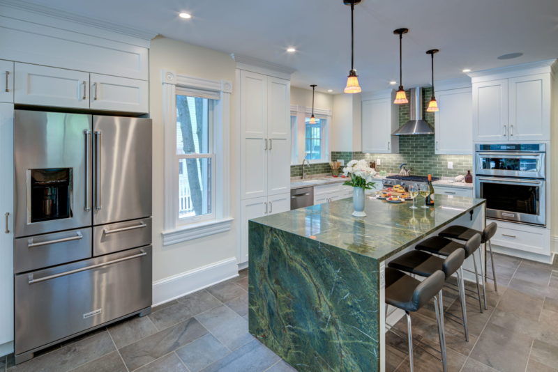kitchen with large waterfall island, green and white counter tops, green subway tile, and white cabinets
